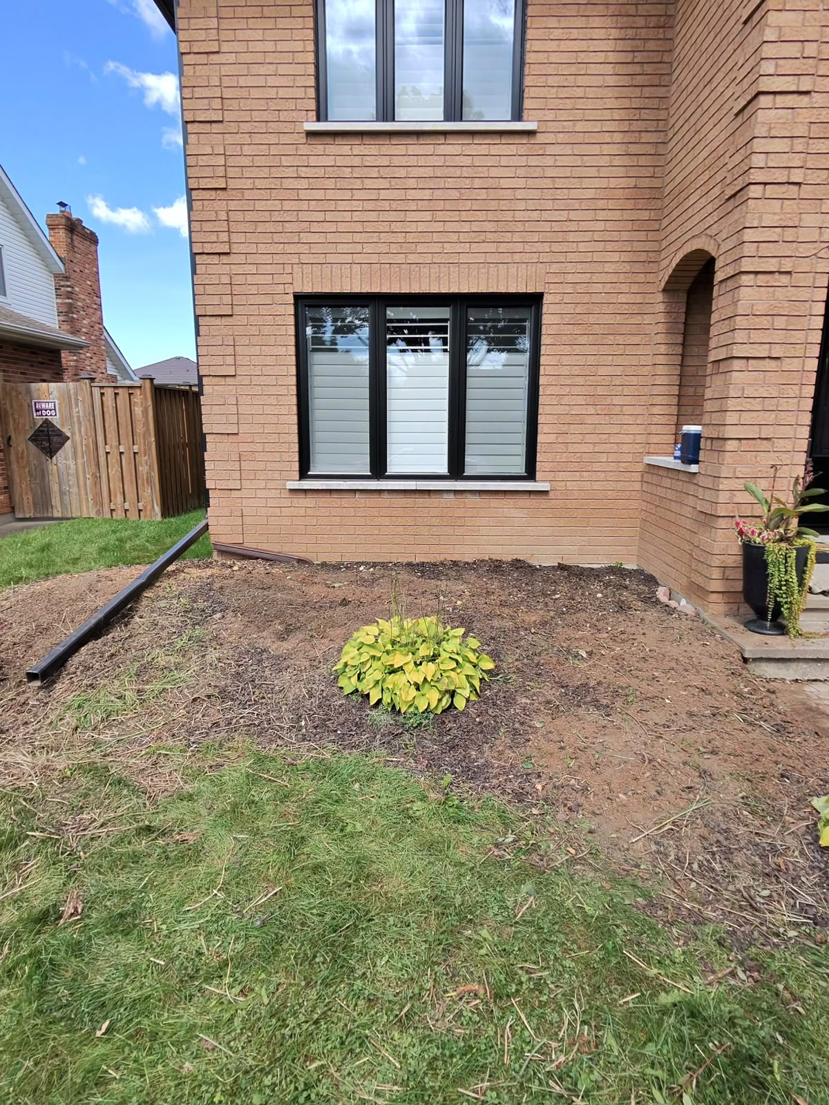 Cleared planting bed beside the same brick home after landscape cleanup